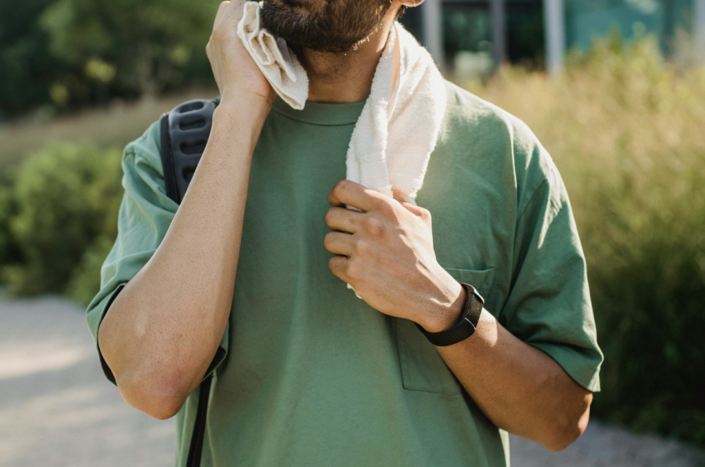 This photo shows a sweating person wiping their face with a towel outdoors.