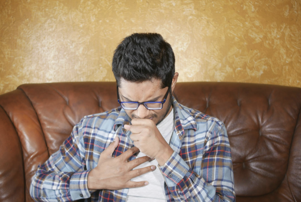 This photo shows a man coughing with one hand on his mouth and chest.