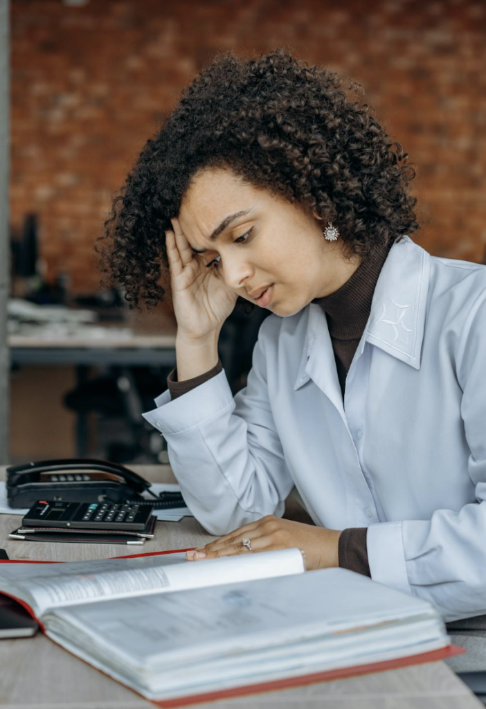 This photo shows a woman sitting at a desk, looking stressed while working.