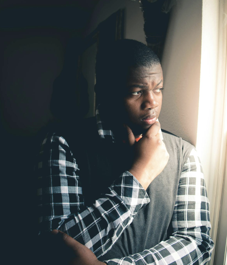 This photo shows a thoughtful person standing near a window with sunlight.