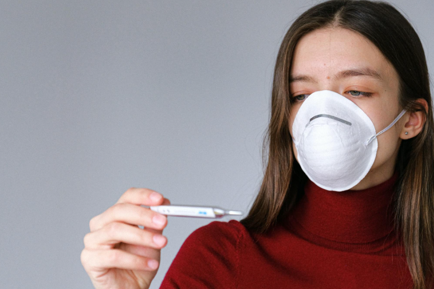 This image shows a woman in a face mask checking a thermometer.