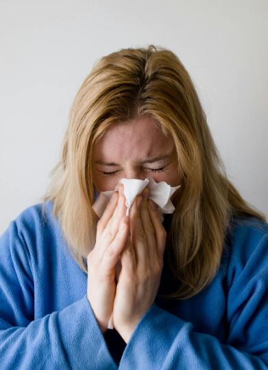 This image shows a sick woman wiping her nose with tissue.