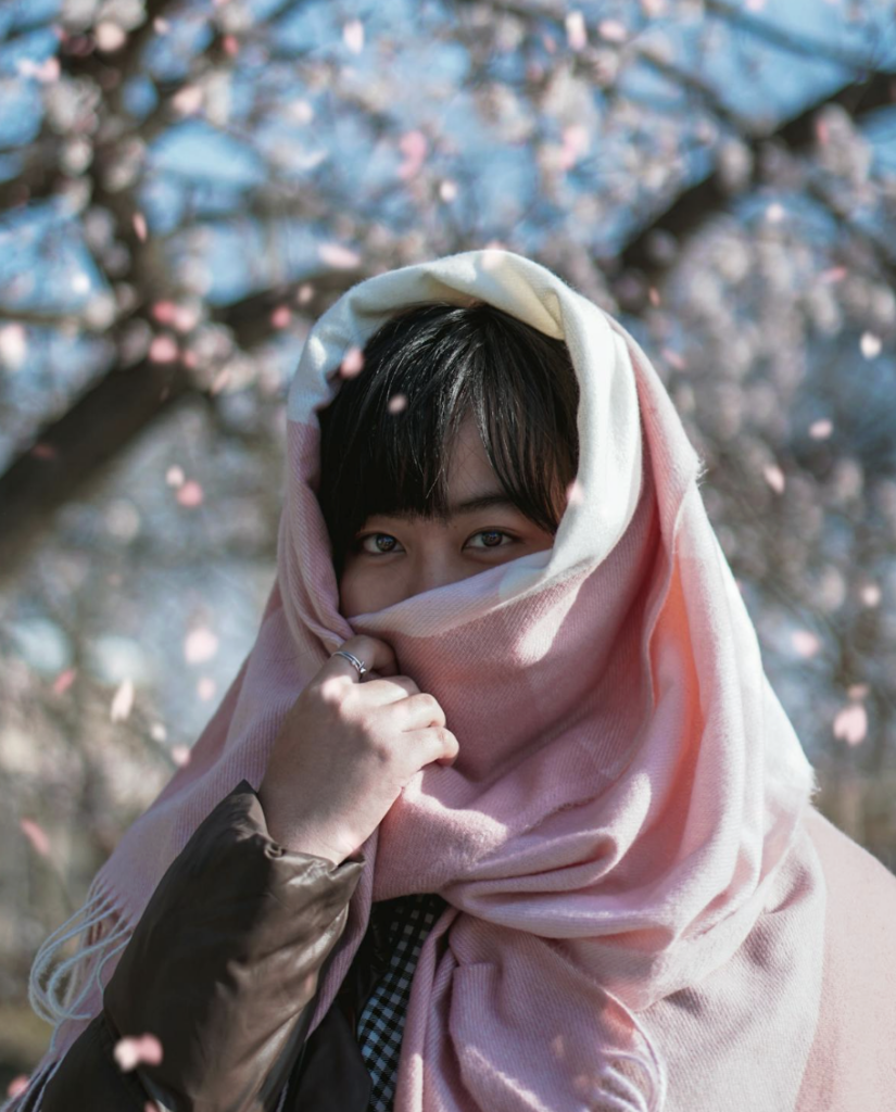 This photo shows a woman covering her face with a shawl outdoors.